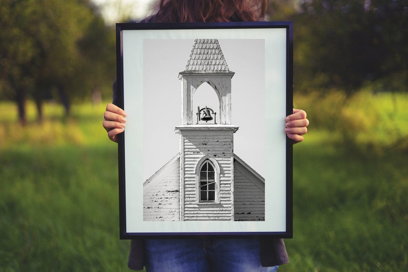 May include: A framed black and white photograph of a weathered church steeple with a bell in the belfry.