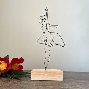 May include: A black wire sculpture of a ballerina in a dancing pose on a wooden base.
