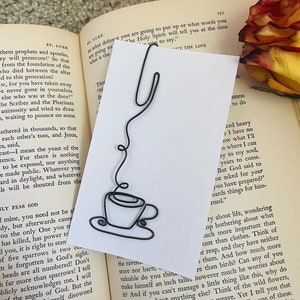 May include: A black wire bookmark shaped like a coffee cup and a stem. The bookmark is on a white card with text that reads "But God said to be asked for your prepared things for him-rned."