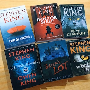Pode incluir: Uma coleção de livros de bolso de Stephen King com vários títulos, incluindo "Doctor Sleep", "O Cemitério dos Animais de Estimação", "A Loteria de Salem", "A Metade Sombria", "Belezas Adormecidas" e "Fim da Vigília".