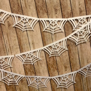 May include: White paper spiderweb garland with a wood background. The garland is made of multiple paper spiderwebs connected together.