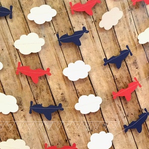 Pode incluir: Uma guirlanda de avi&otilde;es de papel vermelho, branco e azul com avi&otilde;es de papel e nuvens. A guirlanda &eacute; perfeita para um ch&aacute; de beb&ecirc; ou uma festa de anivers&aacute;rio.
