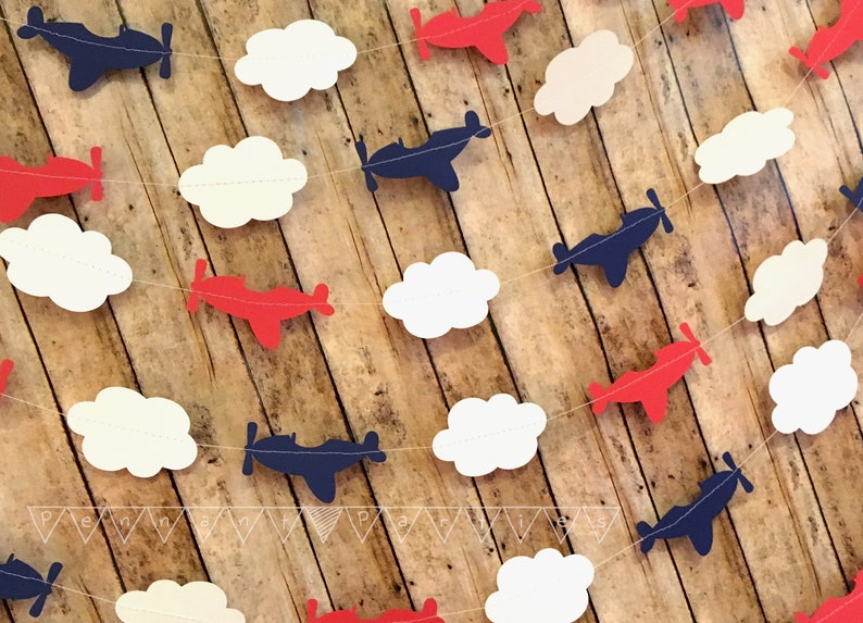Pode incluir: Uma guirlanda de avi&otilde;es de papel vermelho, branco e azul com avi&otilde;es de papel e nuvens. A guirlanda &eacute; perfeita para um ch&aacute; de beb&ecirc; ou uma festa de anivers&aacute;rio.