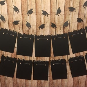 May include: A graduation banner with black mortarboard cutouts strung above black rectangular signs. The signs are labeled with the words "Freshman", "Sophomore", "Junior", and "Senior". The background is a wooden plank wall.