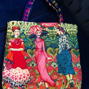 Puede incluir: Una bolsa de mano colorida con un patrón floral y tres figuras. Las figuras son una mujer con un vestido rojo, una mujer con un vestido rosa y un esqueleto con un sombrero negro. La bolsa tiene una correa azul y verde.