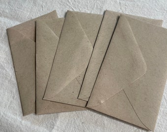 May include: A collection of small, light brown paper envelopes arranged on a textured, off-white surface. The envelopes are closed and have a simple, classic design, suitable for various uses like invitations or notes.