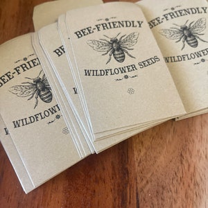 May include: A stack of brown paper envelopes with a bee-friendly wildflower seed design. The envelopes feature a black and white illustration of a bee with the text "Bee-Friendly Wildflower Seeds".