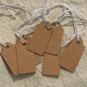 May include: A set of eight brown paper gift tags with white string attached. The tags are blank and ready to be written on.