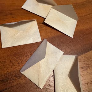 May include: Five white envelopes with a textured surface. The envelopes are folded and ready to be used for sending letters or notes.