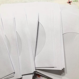 May include: A stack of white envelopes with a circular cut-out on the front. The envelopes are stacked neatly and are ready to be used for mailing.