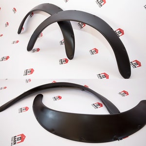 Puede incluir: Cuatro aletas de guardabarros negras, diseñadas para un vehículo, se muestran sobre un fondo blanco. Las aletas tienen una forma curva con agujeros pretaladrados para el montaje. El logotipo "BARN TUNING" es visible.