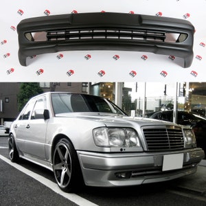 Peut inclure: Pare-chocs de voiture noir avec une grille et des ouvertures d'a&eacute;ration, pr&eacute;sent&eacute; sur fond blanc. L'image inf&eacute;rieure montre une voiture argent&eacute;e avec le pare-chocs install&eacute;, gar&eacute;e dans la rue. La voiture a des roues noires.