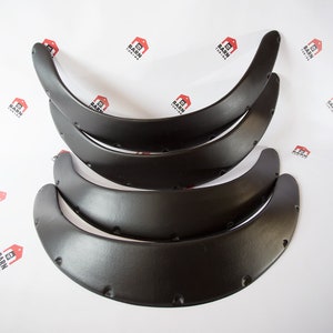 Peut inclure: Ensemble de quatre élargisseurs d'ailes noirs, incurvés et conçus pour l'automobile. Chaque élargisseur comporte plusieurs trous pré-percés pour le montage. Les élargisseurs sont disposés en pile sur fond blanc.