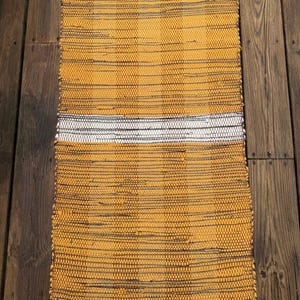 May include: A woven rug with a yellow and brown striped pattern and a white stripe across the middle. The rug has a blue border.
