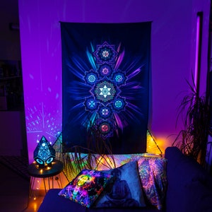May include: A black tapestry with a vibrant, geometric design in shades of blue, purple, and green hangs on a wall. The room is illuminated with purple lighting, and decorative pillows with similar designs are on a dark blue couch.