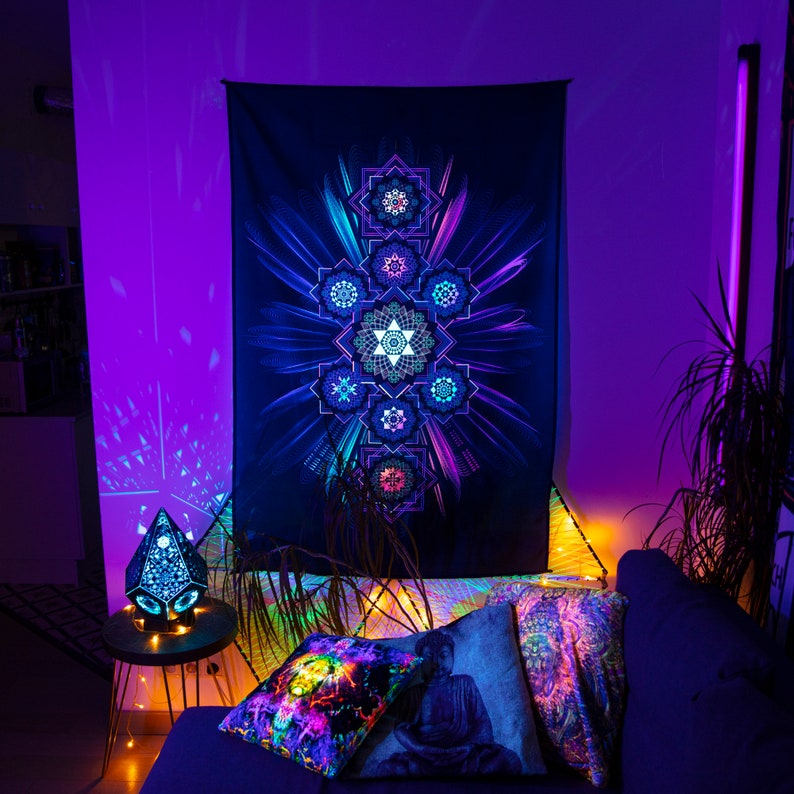 May include: A black tapestry with a vibrant, geometric design in shades of blue, purple, and green hangs on a wall. The room is illuminated with purple lighting, and decorative pillows with similar designs are on a dark blue couch.
