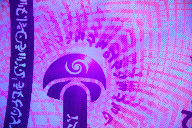 Puede incluir: Una tela morada y blanca con un dise&ntilde;o de hongo. El hongo tiene un dise&ntilde;o de espiral en la parte superior y el texto "Shroom Queens" est&aacute; impreso en la tela.
