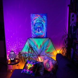 May include: A psychedelic tapestry with a geometric design hangs above a couch with colorful throw pillows. The tapestry is green, blue, and purple, and the pillows are a mix of colors. The room is lit with colorful lights, creating a vibrant and colorful atmosphere.