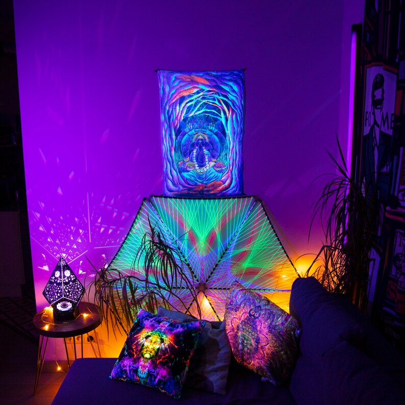 May include: A psychedelic tapestry with a geometric design hangs above a couch with colorful throw pillows. The tapestry is green, blue, and purple, and the pillows are a mix of colors. The room is lit with colorful lights, creating a vibrant and colorful atmosphere.