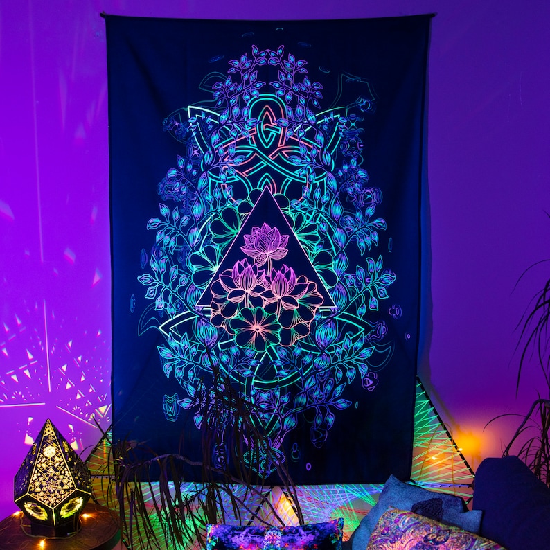 May include: A black tapestry with a glowing, neon-colored design of a lotus flower inside a triangle surrounded by a circular pattern of leaves. The tapestry is hanging on a wall with a purple background.