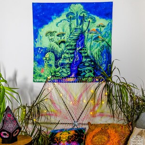 May include: A psychedelic tapestry featuring a glowing blue and green landscape with a staircase leading up to a mushroom forest. The tapestry is hanging on a white wall and is illuminated by string lights.