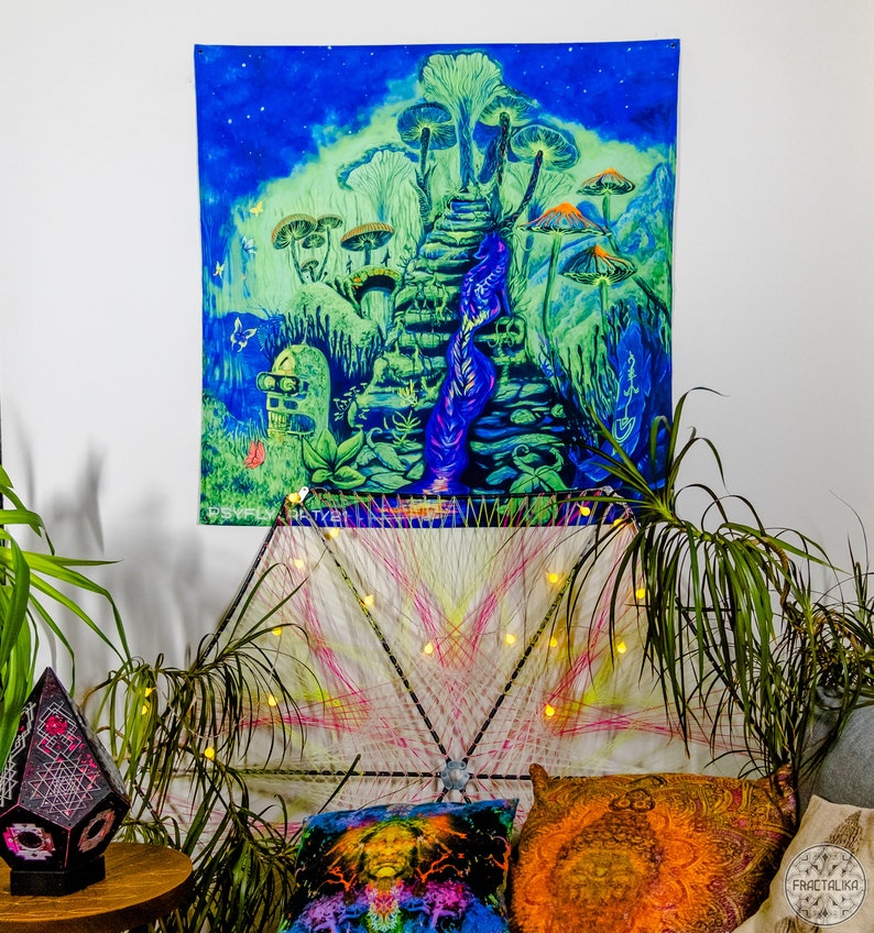 May include: A psychedelic tapestry featuring a glowing blue and green landscape with a staircase leading up to a mushroom forest. The tapestry is hanging on a white wall and is illuminated by string lights.