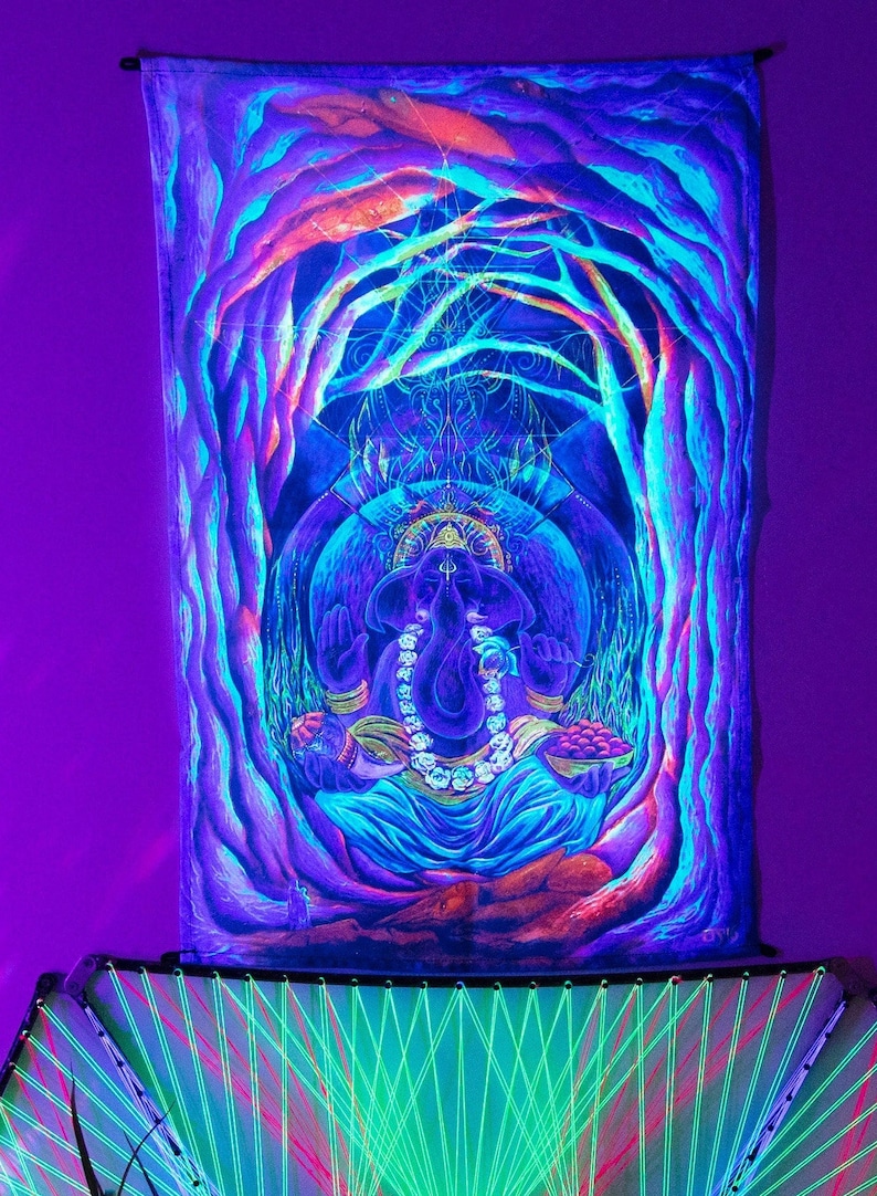 May include: Blacklight tapestry featuring a colorful depiction of the Hindu deity Ganesha, sitting in a meditative pose with a blue background and surrounded by trees. The tapestry is illuminated with a vibrant purple glow.