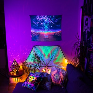 Puede incluir: Una sala de estar de estilo bohemio con un tapiz de pared morado y verde, una luz de cadena y una variedad de almohadas coloridas en un sof&aacute;.