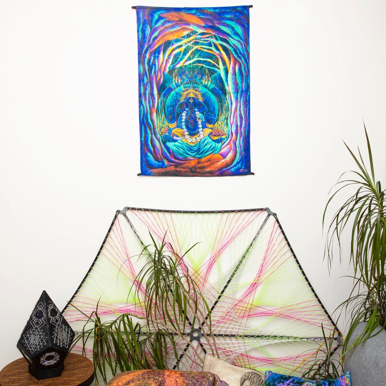 May include: A colorful tapestry with a psychedelic design featuring a deity sitting in a lotus position surrounded by trees and vines. The tapestry is hanging on a white wall above a string art piece.