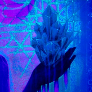 May include: A hand holding a large, blue crystal with a geometric shape. The hand and crystal are silhouetted against a background of purple and blue.