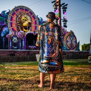 May include: A person wearing a patterned kimono with a detailed design featuring a blue deity figure. The background shows a stage with a large lion head sculpture and vibrant lighting, suggesting a festival or concert setting.