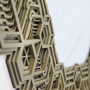 May include: A close-up of a decorative wall mirror with a geometric design. The mirror is made of a light brown material and has a intricate pattern of overlapping hexagons.