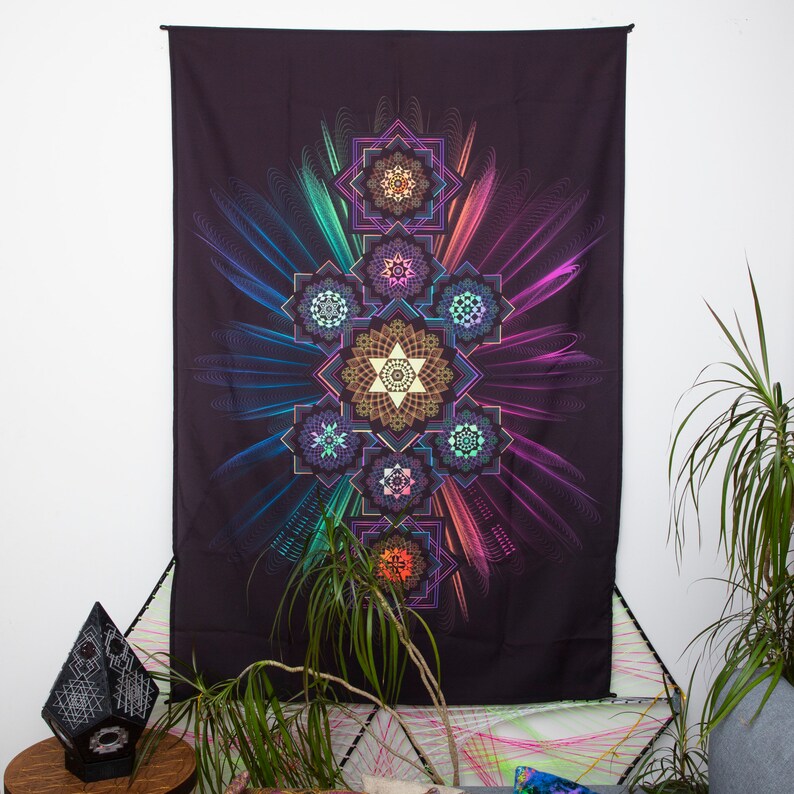 May include: A large, dark tapestry with a vibrant, geometric design. The central pattern features layered star shapes and circular motifs in shades of gold, teal, purple, and pink. The background is black, with colorful, radiating lines.