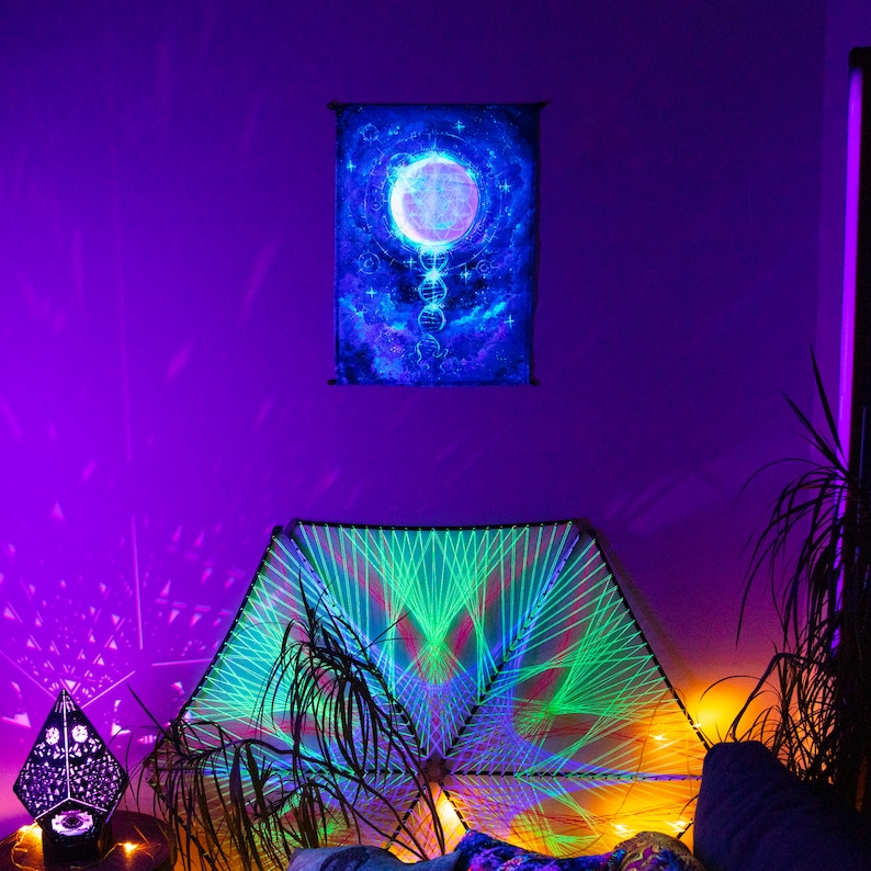 May include: A room decorated with a green and blue string art mandala, a black and white geometric light projector, and a tapestry with a glowing moon and stars. The walls are painted a deep purple.
