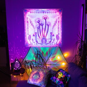 Puede incluir: Un tapiz con un dise&ntilde;o psicod&eacute;lico que presenta hongos y el texto "Shroom Queens". El tapiz est&aacute; colgado en una pared con una luz morada y verde brillando sobre &eacute;l.