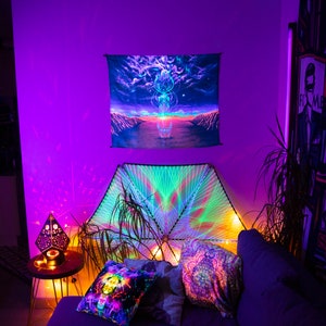 Puede incluir: Una habitaci&oacute;n morada con un sof&aacute;, almohadas y un tapiz colgado en la pared. El tapiz es un dise&ntilde;o psicod&eacute;lico con un esquema de colores arco&iacute;ris. El sof&aacute; est&aacute; cubierto con una tela oscura y tiene algunas almohadas encima. Las almohadas tambi&eacute;n son de dise&ntilde;o psicod&eacute;lico y tienen un esquema de colores arco&iacute;ris.