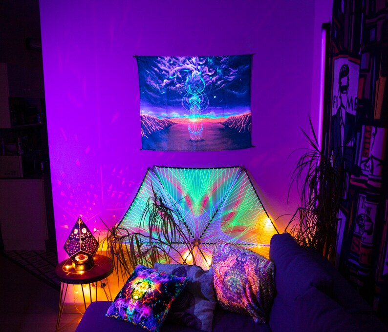 Puede incluir: Una habitaci&oacute;n morada con un sof&aacute;, almohadas y un tapiz colgado en la pared. El tapiz es un dise&ntilde;o psicod&eacute;lico con un esquema de colores arco&iacute;ris. El sof&aacute; est&aacute; cubierto con una tela oscura y tiene algunas almohadas encima. Las almohadas tambi&eacute;n son de dise&ntilde;o psicod&eacute;lico y tienen un esquema de colores arco&iacute;ris.