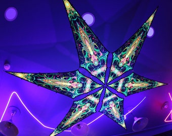 Puede incluir: Una decoración de techo en forma de estrella de seis puntas con un patrón psicodélico en tonos de verde, rosa y amarillo. La estrella está colgada de un techo con luces de neón moradas y rosas.