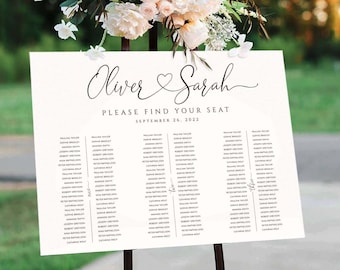 May include: White wedding seating chart with black calligraphy text. The names "Oliver & Sarah" are at the top with a heart symbol between them. The text "Please find your seat" is below the names. The date "September 26, 2022" is below the text. The chart lists guest names in three columns.
