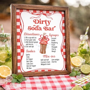 May include: A framed sign with a red and white checkered border, advertising a "Dirty Soda Bar." The sign lists directions, syrups, sodas, and mix-ins. The image includes a Coca-Cola logo and is surrounded by drinks and garnishes.