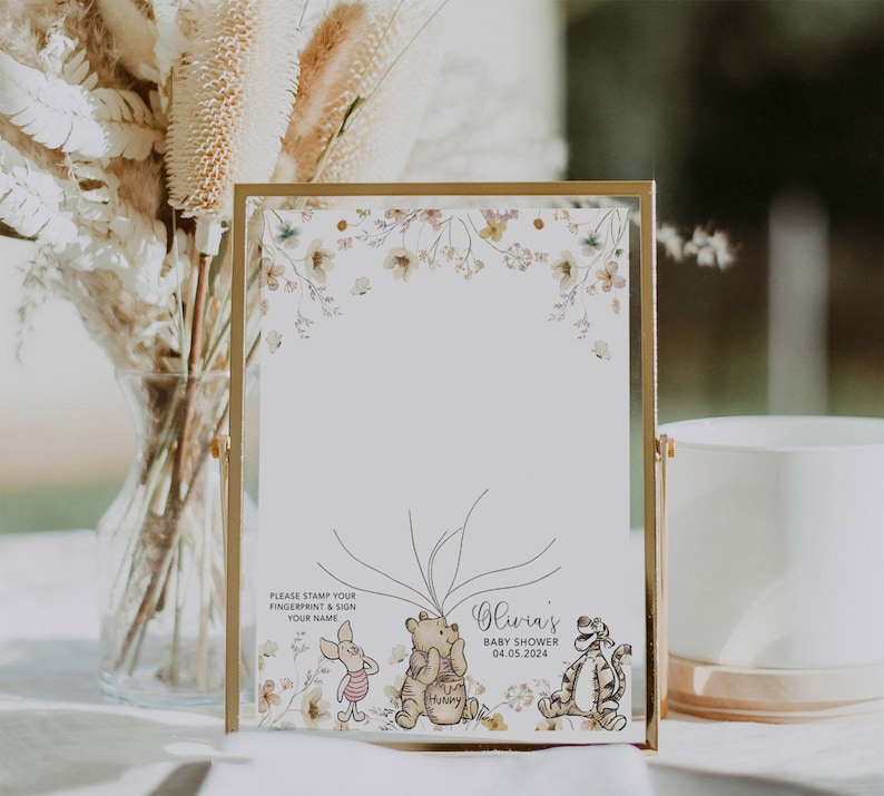May include: A Winnie the Pooh themed baby shower guest book with a floral border. The guest book has a white background with a space for guests to sign their names and leave fingerprints. The text on the guest book reads "Please stamp your fingerprint & sign your name" and "Olivia's Baby Shower 04.05.2024".