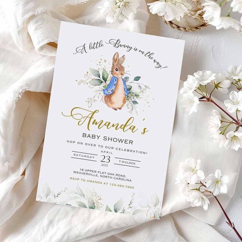Peut inclure: Une invitation de f&ecirc;te pr&eacute;natale blanche avec une illustration aquarelle d'un lapin portant une veste bleue. L'invitation indique "A little Bunny is on the way!" et "Amanda's Baby Shower". L'invitation comprend la date, l'heure et le lieu de la f&ecirc;te.