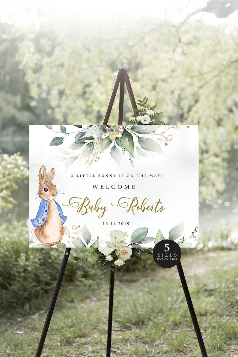 May include: A welcome sign for a baby shower with a watercolour illustration of a bunny rabbit wearing a blue jacket and a floral border. The text reads "A little bunny is on the way! Welcome Baby Roberts 10.14.2019".
