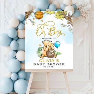 May include: Winnie the Pooh themed baby shower welcome sign with a blue and white watercolor background. The sign says "Oh Boy" in gold script, "Welcome to Olivia's Baby Shower" and the date "06.27.25".