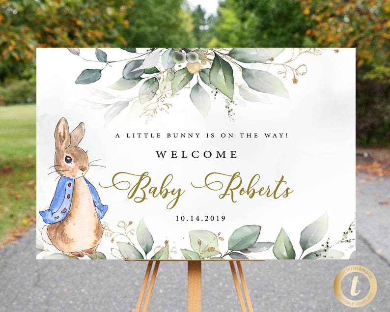 May include: A white welcome sign with a watercolour illustration of a bunny rabbit, green leaves, and gold accents. The text reads "A little bunny is on the way! Welcome Baby Roberts 10.14.2019".