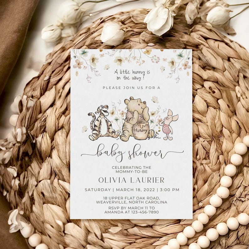 May include: A Winnie the Pooh themed baby shower invitation with a watercolor floral background. The invitation features Winnie the Pooh, Tigger, and Piglet. The text reads "A little hunny is on the way! Please join us for a baby shower celebrating the mommy-to-be Olivia Laurier. Saturday | March 18, 2022 | 3:00 PM. 18 Upper Flat Oak Road, Weaverville, North Carolina. RSVP by March 11 to Amanda at 123-456-7890."