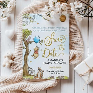 May include: A Winnie the Pooh themed baby shower save the date card with a blue balloon, a quote about the smallest things taking up the most room in your heart, and the text "Save the Date" in gold script. The card also includes the date "24-09-2024" and the text "Amanda's Baby Shower".