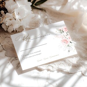 May include: A white RSVP card with gold lettering and a floral design. The text reads "RSVP KINDLY RESPOND BY 04.05.25". The card has checkboxes for accepting or declining the invitation, and for meal choices.
