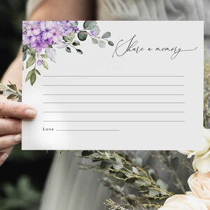 May include: A white card with a floral design in shades of purple and green. The card has the text "Share a memory" written in cursive. There is a blank space for writing and a line for a signature.