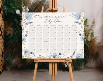 May include: A rectangular sign on a wooden easel featuring a calendar grid with the text GUESS THE DATE OF Baby Olive. The design includes watercolor illustrations of blue flowers, green foliage, and wheat stalks along the left and right borders.
